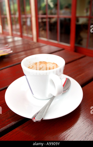 Ein frisch gebrühter Espresso in einer weißen Tasse auf einem Holztisch, perfekt für eine entspannende Kaffeepause in einem Café im Freien. Stockfoto