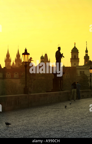 Die goldene Stunde taucht Prags berühmte Karlsbrücke in ein warmes Leuchten, während Statuen mit Silhouetten die ruhige Morgenszene bewachen Stockfoto