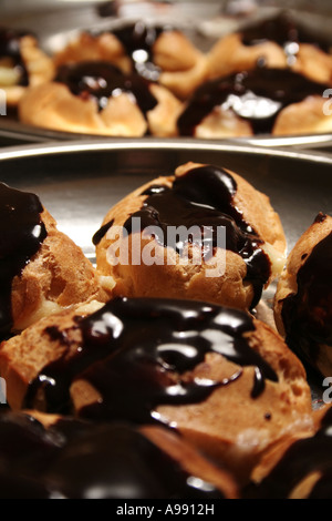 Frische, schokoladenglasierte Profiteroles mit dunkler Ganache, die unter einer glänzenden Beschichtung helles Gebäck im Detail freigeben Stockfoto