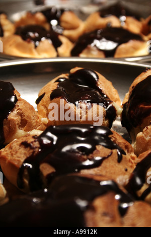 Frische, schokoladenglasierte Profiteroles mit dunkler Ganache, die unter einer glänzenden Beschichtung helles Gebäck im Detail freigeben Stockfoto