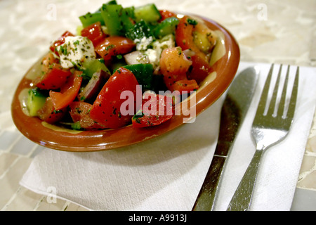 Einen frischen Gemüsesalat mit Tomaten, Gurken, grüner Paprika, Zwiebeln und Fetakäse, serviert in einer Schüssel mit Gabel und Messer an der Seite. Stockfoto