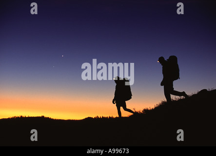 Mann und Frau Silhoutted von der späten Abendlicht Wandern mit Rucksäcken und Scheinwerfer bei Donner Gipfel CA Stockfoto