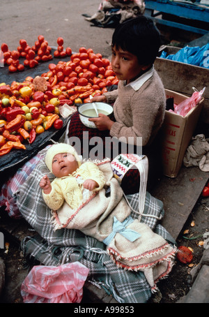 Kleiner Junge isst Suppe bei seiner Mutter Street Automaten Stand, wie er über Säugling Cousin in Huancayo Junin Abteilung Peru Uhren Stockfoto