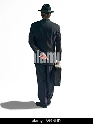 Business-Mann im schwarzen Anzug mit schwarzem Filzhut und Aktenkoffer mit den Fingern hinter dem Rücken gekreuzt Stockfoto