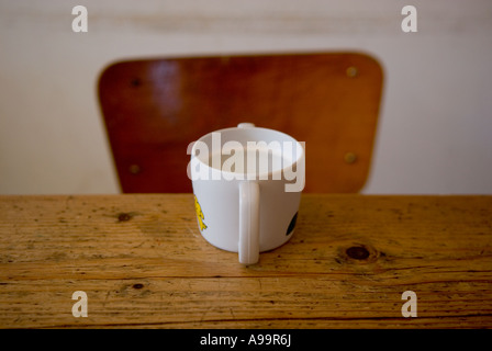 Ein einzelnes Kind Tasse Milch auf einem Küchentisch Kiefer mit einem Stuhl im Hintergrund Stockfoto