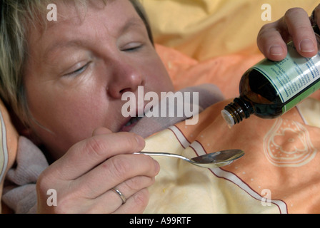 Herr Frau, die kalte Grippe Influenza im Bett liegend unter Tropfen Medizin aus einer Flasche Stockfoto