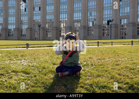 Eine Nahaufnahme eines Kindes mit Superman Maske sitzen auf dem Rasen vor dem modernen Gebäude in Montpellier, Frankreich Stockfoto