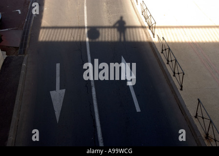 Blick hinunter auf eine zwei zweispurigen Straße mit weißen Richtungspfeile und einen Schatten von jemandem auf einer Brücke Stockfoto