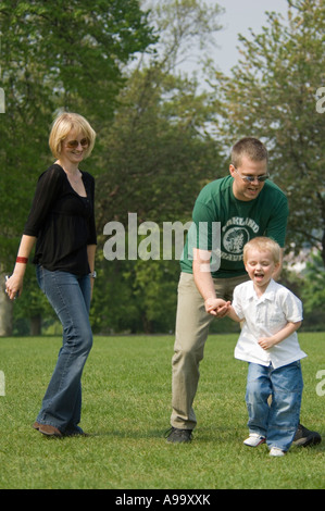 Eine blonde junge und seine Eltern lachen und spielen im Park an einem sonnigen Frühlingstag. Stockfoto