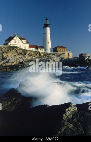 Portland Head Lighthouse in Maine bei Sonnenaufgang mit Wellen, die über felsige Ufer unten Stockfoto