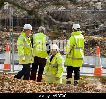Eine Gruppe von Bauherren, die hohe Vis reflektierenden gelben Mänteln und weißen Schutzhelme tragen. Site-Manager.  Straße Zapfen. Baustelle in UK Stockfoto