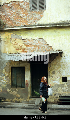 Ältere Frau, die vorbei an alten verfallenden Gebäude, hängen kann Ngang St, Altstadt in Hanoi, Vietnam Stockfoto