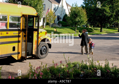 Mama zu Fuß Sohn über Straße und winken ade Schulbusfahrer. St Paul Minnesota MN USA Stockfoto