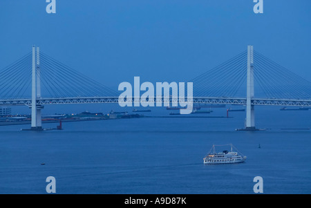 Ein Kreuzfahrtschiff vor Yokohama Bay Bridge in der Dämmerung Stockfoto