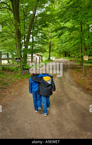 zwei jungen twin Brüder hinunter unbefestigte Straße umgeben von bewaldeten Gebiet zusammen Arm in arm Stockfoto
