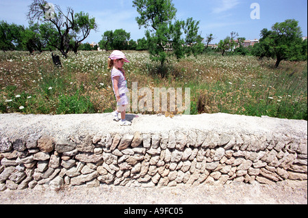 Ein Mädchen geht entlang einer Wand an der Stelle der römischen Ruinen in Alcudia auf Mallorca Stockfoto