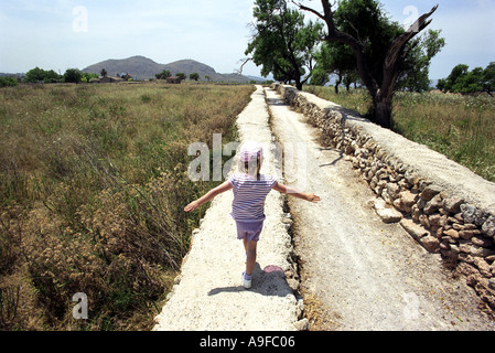 Ein Mädchen geht entlang einer Wand an der Stelle der römischen Ruinen in Alcudia auf Mallorca Stockfoto