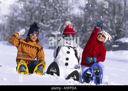 zwei Mädchen tragen Schneeschuhe, saß ein Schneemann, Schneebälle zu werfen. Stockfoto