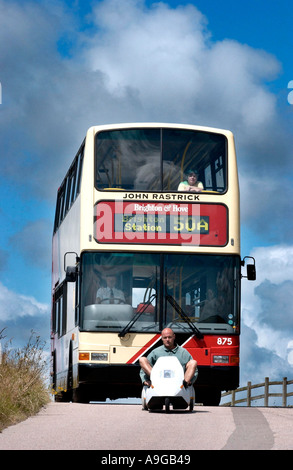 Ein Doppeldecker-Bus wartet geduldig auf einen unterlegenen Sinclair C5 auf die Braue des Hügels crest Stockfoto