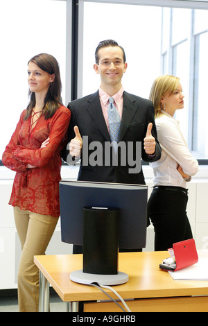 lächelnder Mann stehend im Büro zwischen zwei Frauen Stockfoto