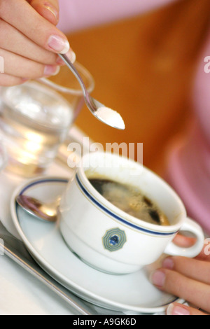 weibliche Hand streuend Zucker in einer Tasse Kaffee. Stockfoto