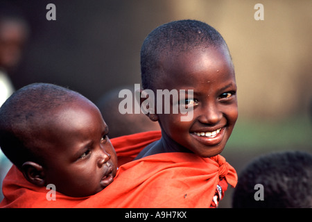 Ein Junge Masai-Mädchen trägt ein Kind auf dem Rücken in der Masai Mara-Region Kenias. Stockfoto