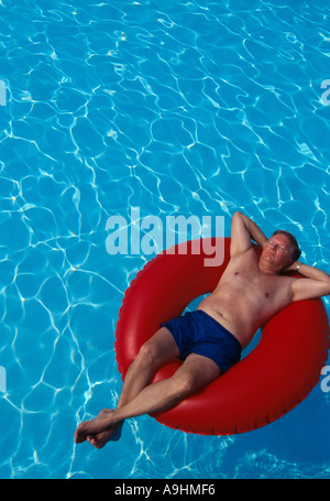 Mittleren Alter Männermodel entspannt in einem Pool auf einem roten Schlauch Stockfoto