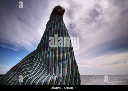 kleiner Junge stand am Strand mit einem Handtuch um sich selbst gewickelt Stockfoto