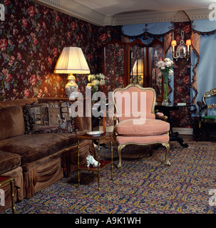 Braun samt Couch und rosa Sessel in achtziger Jahre Wohnzimmer mit gemusterten Tapeten und Teppich Stockfoto