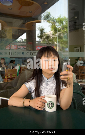 PORTRÄT-MODELL VERÖFFENTLICHT JUNGE MITTELSCHICHT CHINESIN MIT HANDY IN STARBUCKS CAFE PEKING CHINA Stockfoto