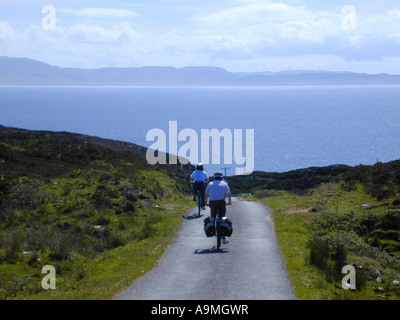 Zwei Radfahrer auf eine asphaltierte Straße auf der Insel Colonsay mit Isle of Jura im Hintergrund Stockfoto