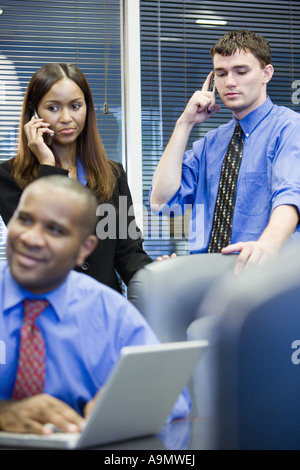 Business-Mann und Frau mit Handy, während Kollege Laptop-Computer im Vordergrund verwendet Stockfoto