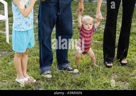 Baby versuchte aufzustehen auf Rasen, Hände statt von seinen Eltern Stockfoto