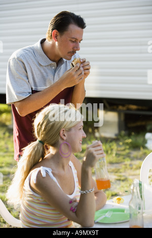 Blick auf ein glückliches Paar, Essen und trinken am eine Grillparty vor einem Anhänger-Haus Stockfoto