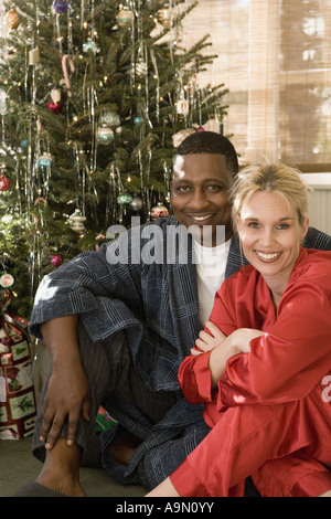 Porträt eines ausgereiften interracial Paares in Pyjamas Weihnachtsbaum sitzen Stockfoto