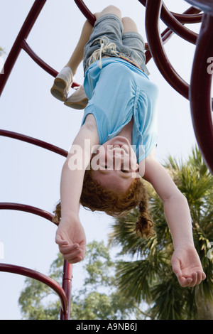 Mädchen hängt kopfüber an Klettergerüst auf einem Spielplatz Stockfoto