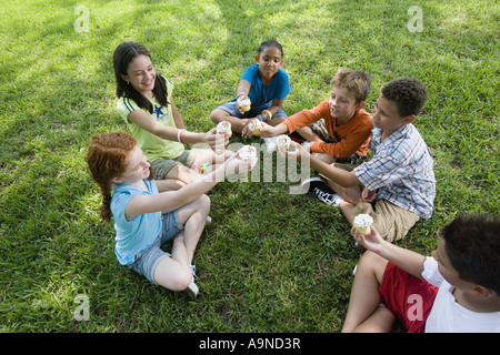 Kinder sitzen in einem Kreis jubeln über Cupcakes in einem park Stockfoto