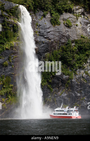 Sprudelnden Wasserfall Kaskaden durch Buchenwald im Fiordland Nationalpark in Neuseeland mit roten Ausflugsboot im Wasserfall-spray Stockfoto