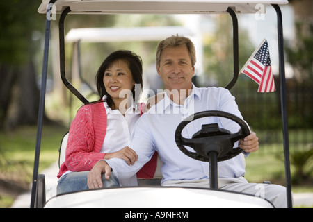 Älteres Inter-racial paar ihren Golfcart durch ihre Nachbarschaft zu fahren Stockfoto
