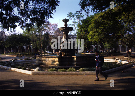 EIN SCHULJUNGE GEHT VORBEI AN EINEM BRUNNEN IN DEN PARQUE CENTRAL VOR DER PALACIO DE LOS CAPITANES ANTIGUA GUATEMALA Stockfoto