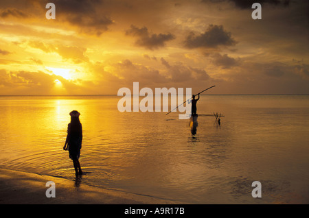 Ausleger-Kanu in Aitutaki Lagune bei Sonnenuntergang mit polynesischen Mädchen in seichtem Gewässer Cookinseln Südsee Stockfoto