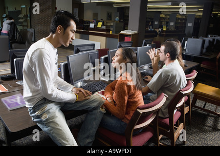 Studenten im Gespräch während der Verwendung von Computern in der Bibliothek Stockfoto