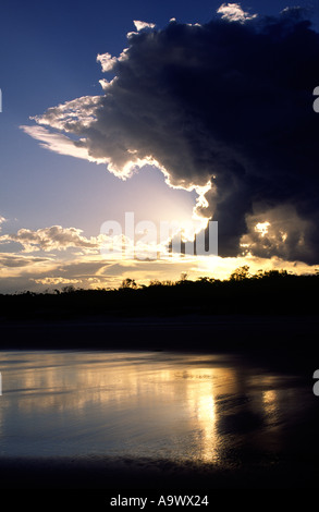 Sonne hinter dunklen Wolken reflektiert im nassen sand Stockfoto