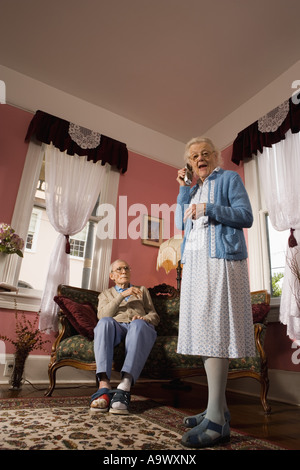 Ältere Frau Gespräche über schnurloses Telefon während mürrischer senior Mann Uhren Stockfoto
