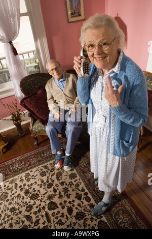 Ältere Frau Gespräche über schnurloses Telefon während mürrischer senior Mann Uhren Stockfoto