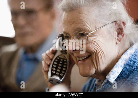 Ältere Frau am schnurloses Telefon mit älteren Mann im Hintergrund Stockfoto