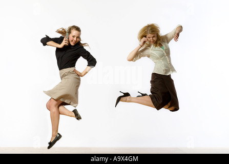 Zwei attraktive junge Frauen konservativ gekleidet in Business-Kleidung in die Luft springen. Man nutzt ein Handy/Gläser Stockfoto