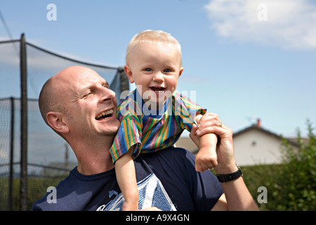 Niedliche Lachen blonde Baby auf seines Vaters Schulter draußen im Garten Familie Spaß Stockfoto