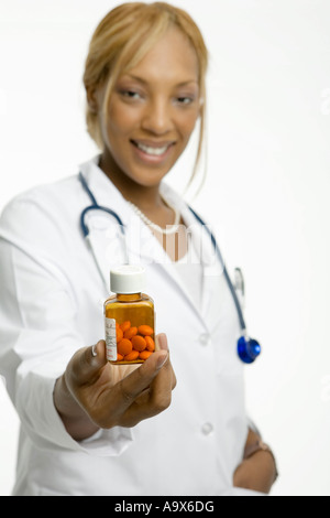 Lächelnde junge Ärztin trägt einen weißen Kittel und ein Stethoskop, ein Patient eine Flasche Pillen anzubieten. Stockfoto