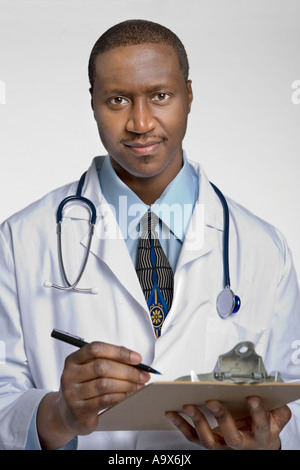 Ein junger schwarzer Doktor ist trägt einen weißen Mantel und Patientenergebnisse auf einem Klemmbrett schreiben. Er sieht Inhalt wie auf gute Nachrichten Stockfoto